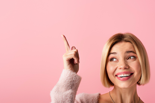 happy young woman in soft cardigan pointing with finger isolated on pink