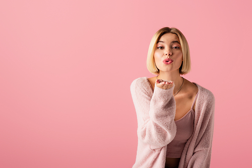 young woman in soft cardigan sending air kiss isolated on pink