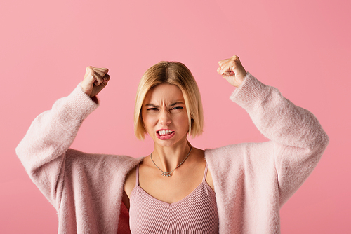 angry young woman in soft cardigan with clenched fists isolated on pink
