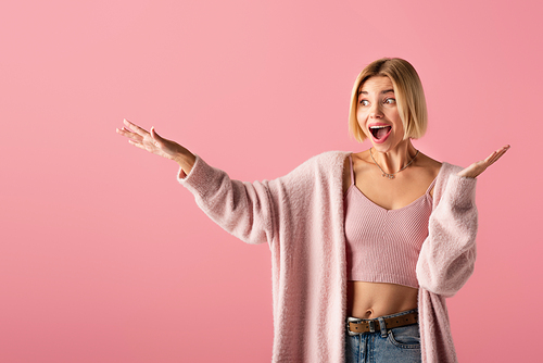 excited young woman in soft cardigan gesturing isolated on pink