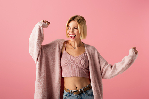 positive young woman in soft cardigan gesturing isolated on pink