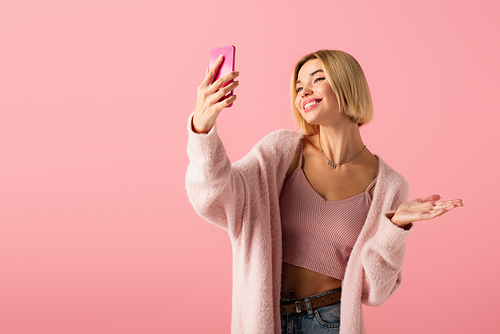 happy young woman in soft cardigan taking selfie isolated on pink