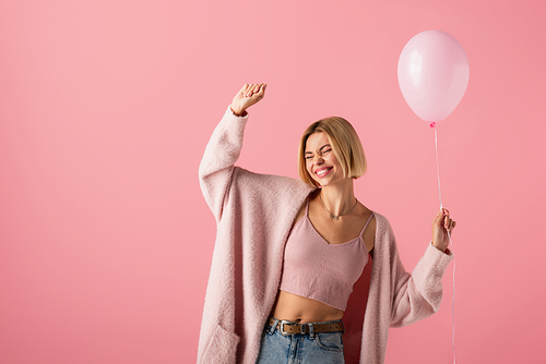 joyful young woman in cardigan holding balloon isolated on pink