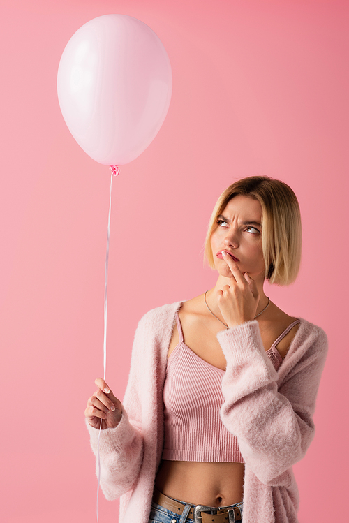 pensive young woman in cardigan holding balloon isolated on pink