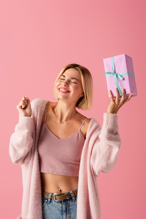 happy young woman with closed eyes holding wrapped gift box isolated on pink