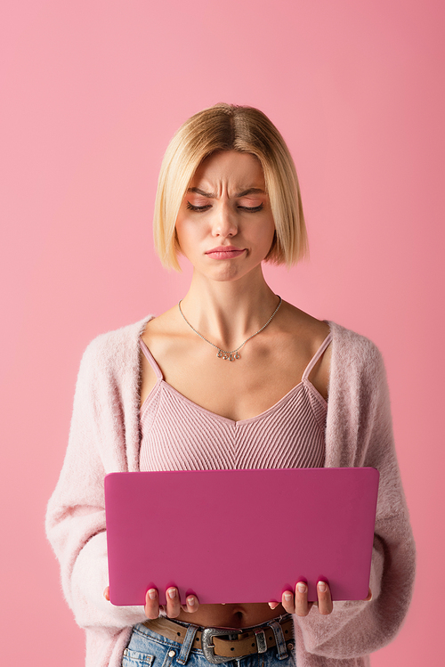 displeased young woman using laptop isolated on pink
