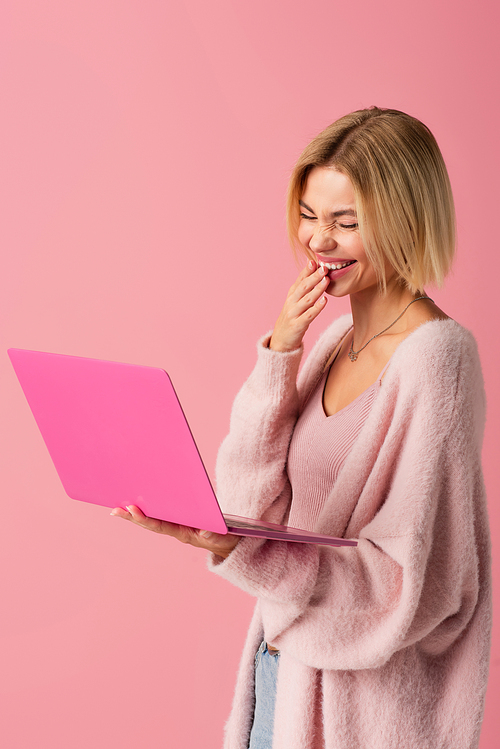 happy young woman using laptop and laughing isolated on pink
