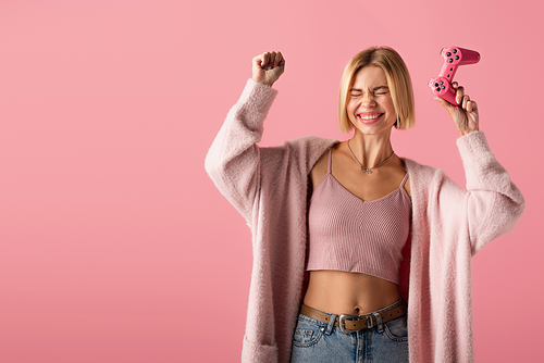 KYIV, UKRAINE - OCTOBER 29, 2021: excited young woman holding joystick isolated on pink