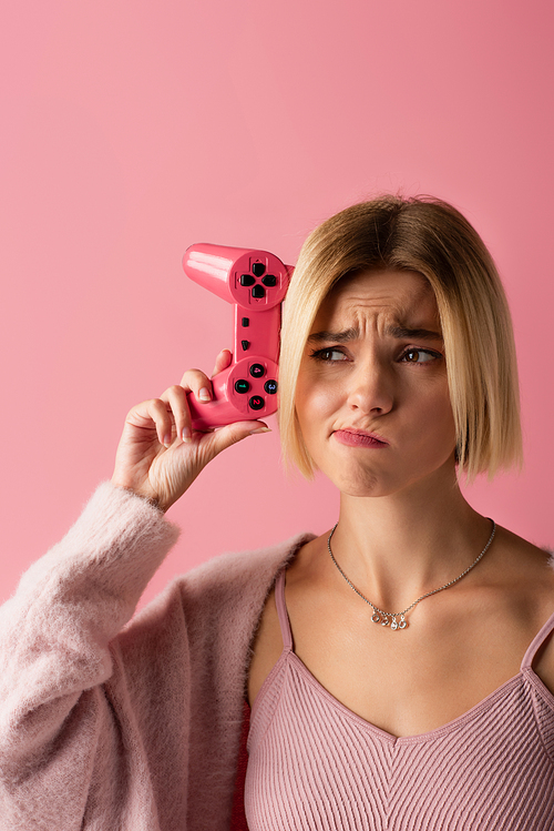 KYIV, UKRAINE - OCTOBER 29, 2021: sad woman holding joystick isolated on pink