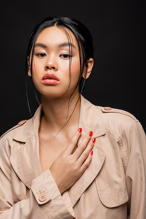 Portrait of stylish asian model in beige trench coat isolated on black