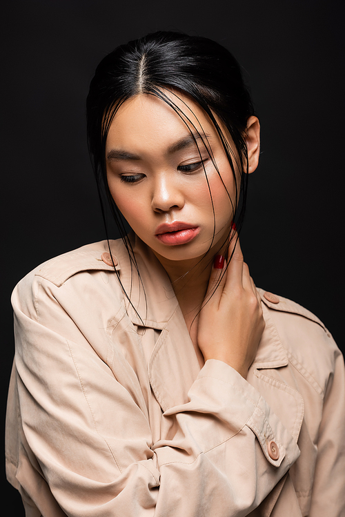 Portrait of pretty asian model in beige trench coat looking away isolated on black