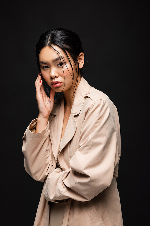 Young asian model in trench coat looking at camera isolated on black