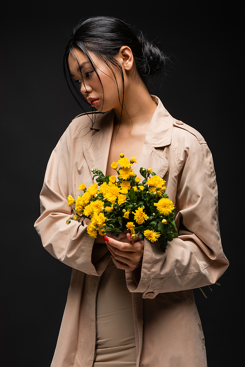 Asian model in beige trench coat holding chrysanthemums isolated on black