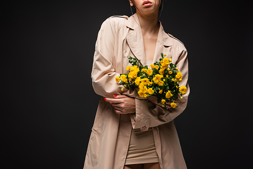 Cropped view of young woman in trench coat holding chrysanthemums isolated on black