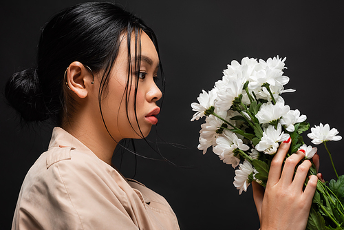 Pretty asian model in trench coat holding white chrysanthemums isolated on black