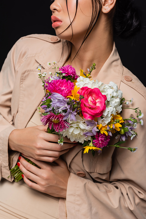 Cropped view of stylish woman in trench coat holding flowers isolated on black