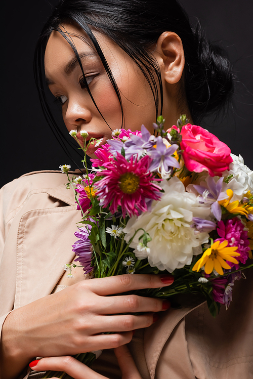 Portrait of asian model in trench coat holding colorful bouquet isolated on black