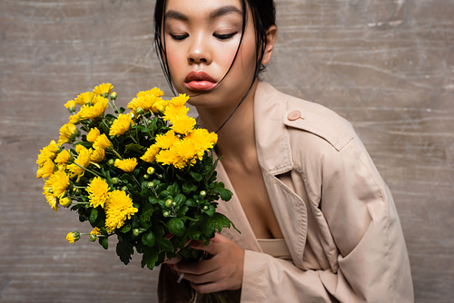 Asian woman in trench coat holding chrysanthemums on abstract brown background