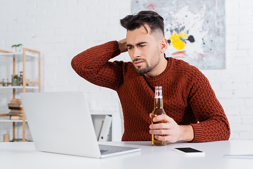 displeased bookmaker with bottle of beer looking at blurred laptop