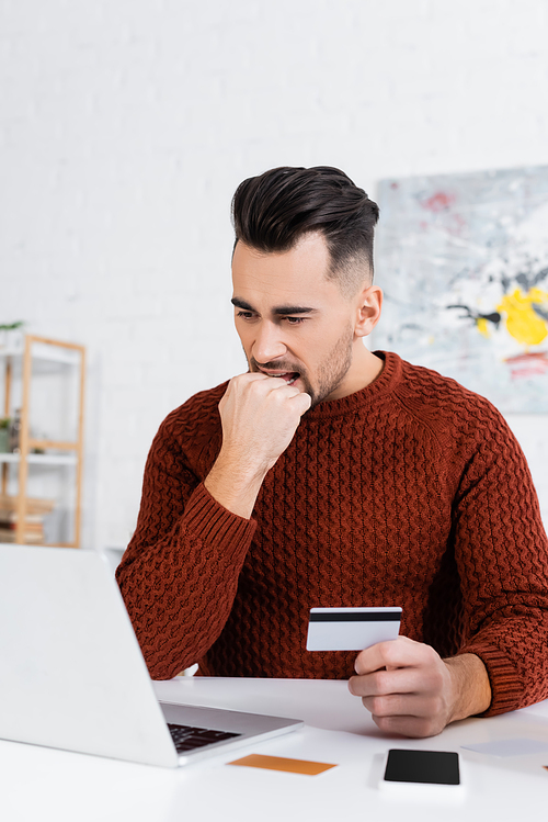 nervous bookmaker biting fist while holding credit card near laptop