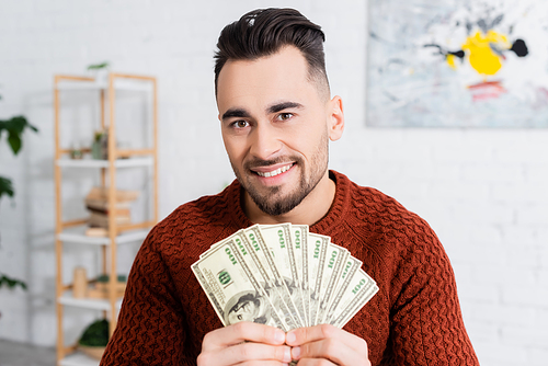 cheerful bookmaker looking at camera and showing dollar banknotes