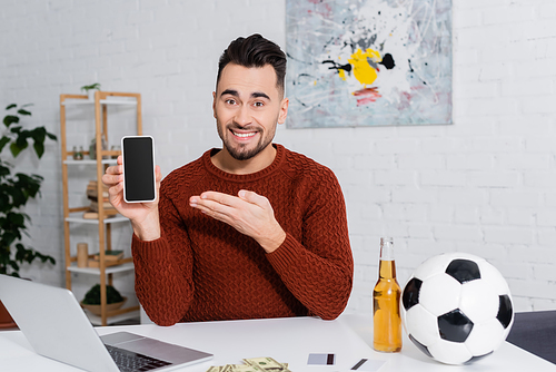 cheerful gambler with soccer ball near credit cards and laptop with sports game on screen