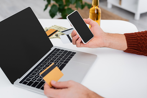 cropped view of gambler with credit card and cellphone near laptop with blank screen