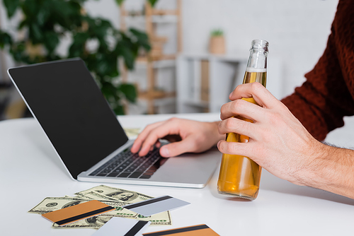 cropped view of bookmaker with bottle of beer near laptop, money and credit cards