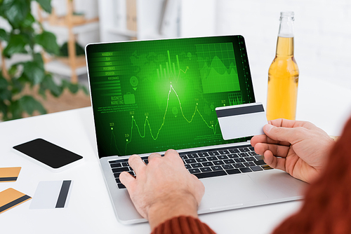 partial view of bookmaker holding credit card near laptop with infographics on screen