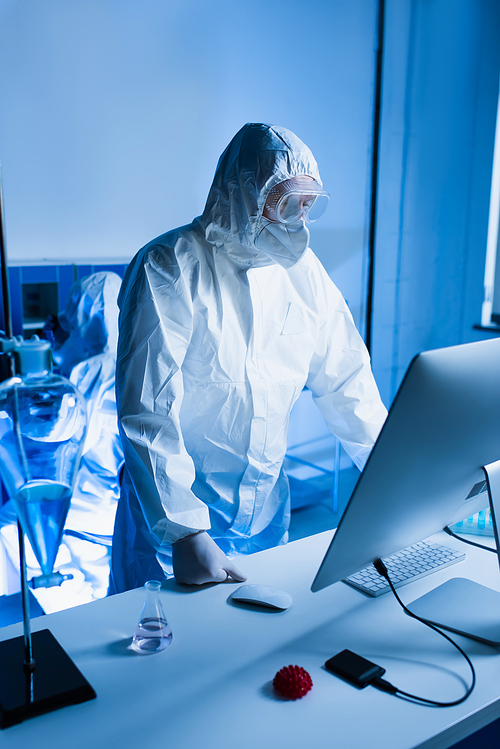 scientist in hazmat suit standing near computer monitor in lab