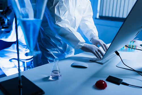 cropped view of virologist in latex gloves typing on keyboard near flask with liquid