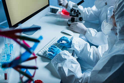 bioengineers in hazmat suits working near computer monitor with grey screen in laboratory