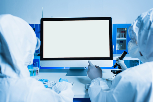 back view of scientist pointing at monitor with white screen near colleague in lab