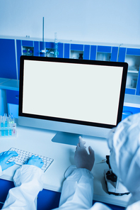 cropped view of scientist in latex gloves pointing at monitor with white screen while colleague typing on keyboard