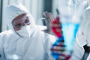 virologist in medical mask and goggles showing petri dish to blurred colleague
