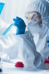 blurred virologist holding test tube near model of coronavirus bacteria