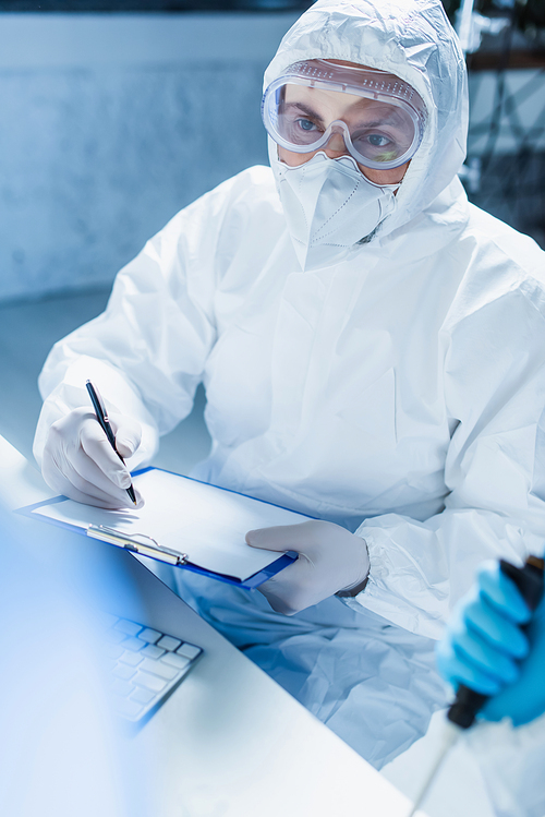 geneticist in hazmat suit holding blank clipboard and pen in lab