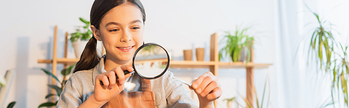 Cheerful kid holding tweezers with plant and magnifying glass at home, banner