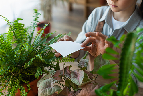 Cropped view of girl holding sticky note near plants at home