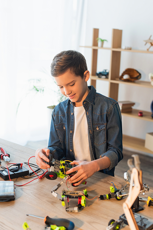 Happy preteen boy making robotic model near tools on table at home