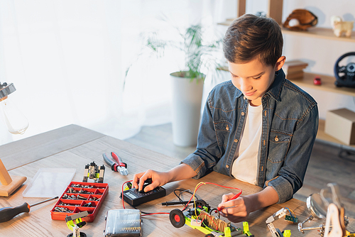 Preteen boy making robotic model with millimeter near tools and screws at home