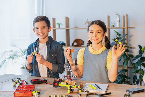 Happy kids holding tools near robotic model on table at home