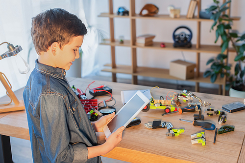 smiling preteen boy with digital tablet near tools and details of robotics model on table