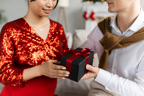 partial view of pregnant woman in red and shiny clothing taking Christmas present from husband