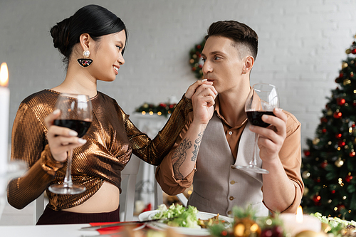 tattooed man kissing hand of elegant asian wife while celebrating Christmas at home