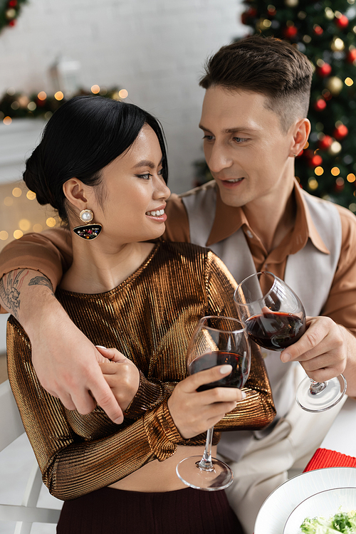 elegant multiethnic couple clinking wine glasses during festive romantic supper at home