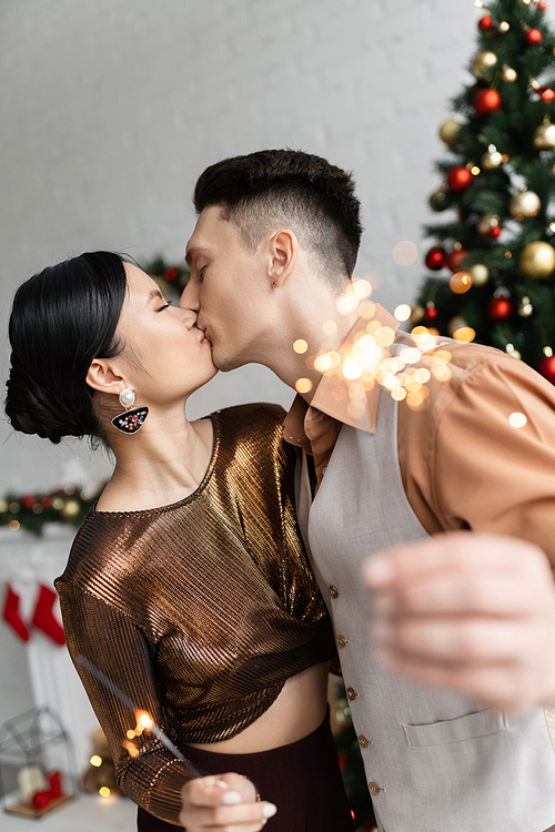 elegant interracial couple holding festive sparklers and kissing with closed eyes