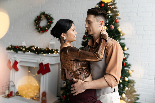 young interracial couple in festive outfits hugging near Christmas tree