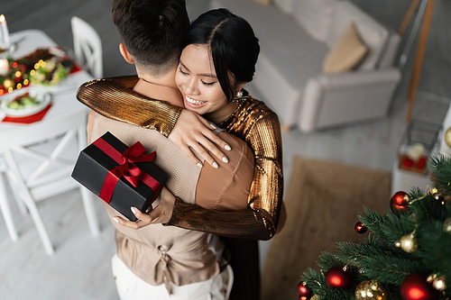 high angle view of cheerful asian woman hugging husband while holding Christmas present