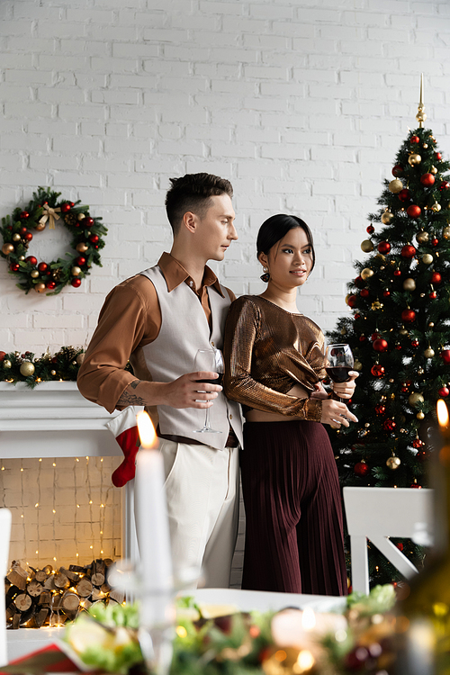 multiethnic husband and wife holding glasses of wine during Christmas celebration